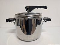Front view of stainless pressure cooker with lid locked, showing handles and reflective finish
