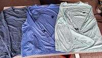 Three shirts laid out: steel blue waffle henley, heather blue crew, light mint crew