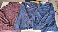 All three tops laid flat: maroon hoodie, navy henley, navy sweater
