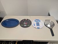Four items laid out: blue platter, two Star Wars plates, metal press