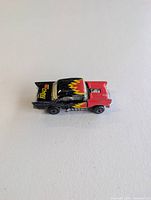 Top view of Matchbox 57 Chevy die-cast car showing red front, black rear, yellow flame graphic, opening hood feature
