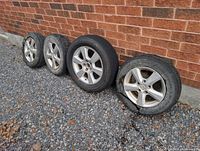 Four Mazda alloy wheels with tires lined against brick wall