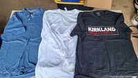 Three shirts laid out: blue polo, white tee, black graphic tee