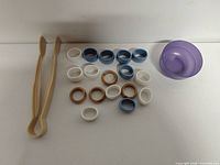 Group shot of all items: napkin rings clustered, tongs left, bowl right