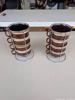 Two vertical stacks of four brown/tan cups each in metal racks