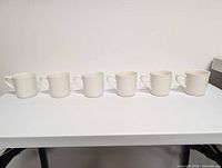 Front view of six matching white ceramic mugs lined up