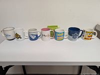 Front view of all eight mugs lined in a row displaying graphics