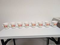 Eight white mugs with floral design lined on table