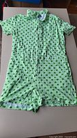 Full view of green/white shamrock print romper laid flat