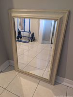 Front view of rectangular mirror with cream and gold frame leaning against wall