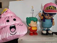 Full view of all three items: Arale figure, Gatchan figure, pink poop plush