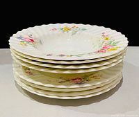 Stack of eight Arcadia plates showing scalloped edges and floral design