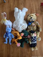 Group of seven Beanie Babies including bunny, blue bear, white laying bear, mottled brown bear, giraffe, dinosaur, beret bear