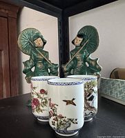 Front view of two green figurines and three porcelain cups on shelf