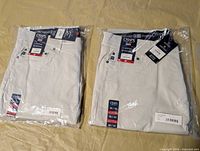 Two sealed pairs of light stone Chaps pants side by side