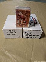 White storage box labelled 97-98 Pacific HKY. Set and box labelled 90-91 Upper Deck Hockey Series 1 with Hockey Canada card set on top