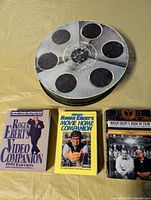 Group shot of three books and round film-reel tin board game