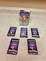 Sealed Lorcana starter deck standing behind five sealed Pokémon Trick or Trade promo packs on countertop