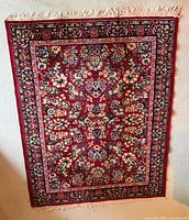 Front view of red floral area rug leaning on wall