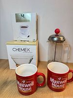 Group shot showing electric beverage warmer box, Chemex filter box, Bonjour French press, two Maxwell House mugs