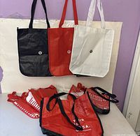 Assorted large and small Lululemon bags in red, black and white displayed on wall hooks and table