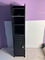Full view of slim black cabinet showing shelves, roll holder, and door