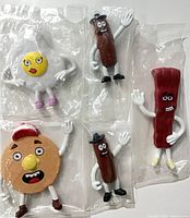 Front view of all five sealed Denny’s breakfast food figurines in bags