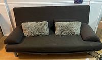 Front view of dark brown IKEA Beddinge Lovas sofa bed with two faux-fur pillows and arm bolsters