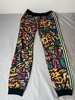 front view of adidas Love Unites track pants showing full graffiti print and side stripes