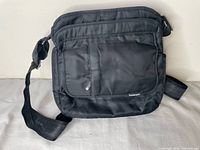 Front view of black Frommer's shoulder bag showing flap, front zip pocket, adjustable strap