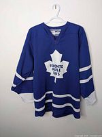 Full front view of blue Toronto Maple Leafs CCM jersey hanging on hanger