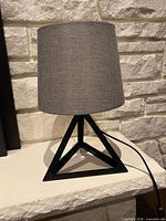 Full view of lamp showing gray fabric shade and black geometric metal base