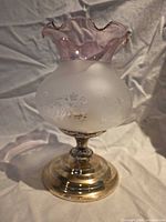 Full view of brass hurricane lamp showing frosted etched glass globe and pink ruffled rim shade