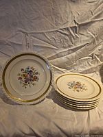 Stack of six plates, showing scalloped rims, gold band, floral centers