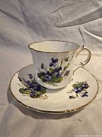 Teacup on saucer showing front violet design and gold trim