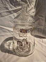 Front view of clear glass jar showing rooster design and gold band