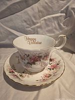 Teacup on saucer showing front floral design and gold script