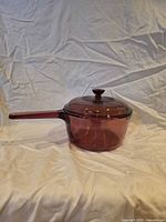 Side view of cranberry glass saucepan with lid attached