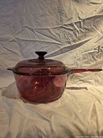 Side view of cranberry glass saucepan with lid on