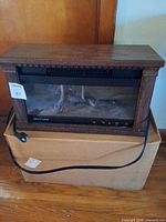 Front view of Heat Surge tabletop electric fireplace heater showing wood finish, glass front, touch controls, attached power cord