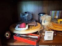 Shelf with lazy susan, glass bowls, spoons in box, glass pitcher and tag