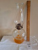 Full view of glass oil lamp beside ruler for scale