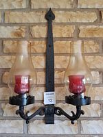 Full view of one sconce mounted on brick wall showing metal frame, glass shades, red candles