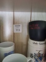 Shelf with Avon mug, Duke University stein and other mugs