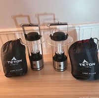Two GE lanterns and two Teton Sports camp pillows in stuffsacks on table
