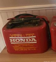 Front view of red Honda gasoline tank showing branding and hose