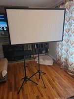 Front view of white 60 in. screen on tripod with Amada stand beside it