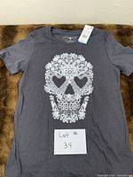Full view of charcoal T-shirt front showing lace skull graphic and hang tag