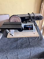 Front view showing Delta ShopMaster branding, sanding disc, belt arm, table and power cord