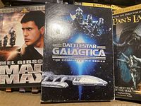 Front of three prominent DVDs: Mad Max, Battlestar Galactica box, Pan’s Labyrinth
